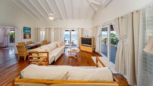 Un amplio salón con suelo de madera, un conjunto de sofás, un televisor y un balcón con vistas al mar.