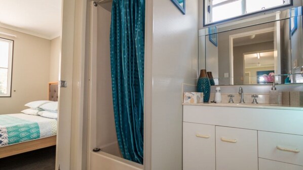 A bedroom with a bed, a bathroom with a shower curtain, and a vanity with a mirror.