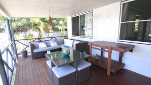 A covered outdoor seating area with a glass table, wicker chairs, and a wooden bench.