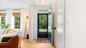 Un couloir doté d’un plancher en bois, d’un canapé blanc, d’un fauteuil en cuir marron et d’une porte donnant sur l’extérieur.