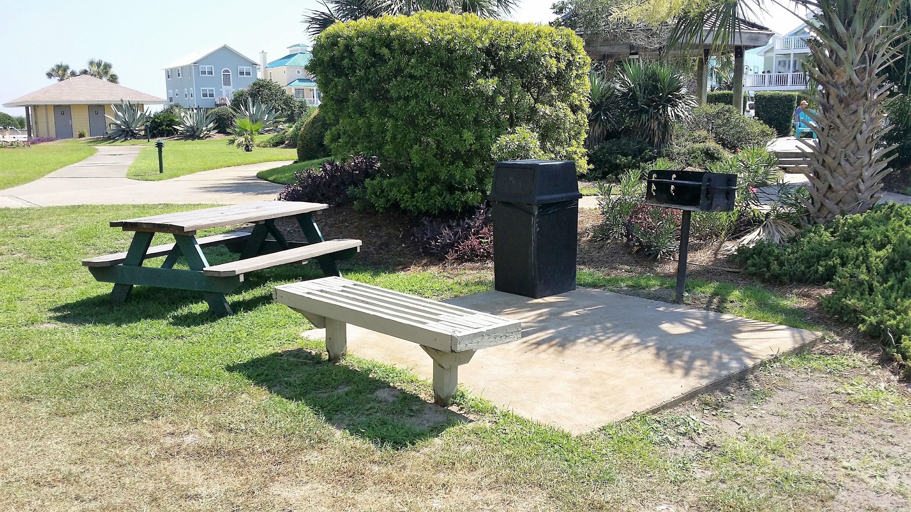 A picnic area with a bench and picnic table, surrounded by well-maintained grass and bushes.