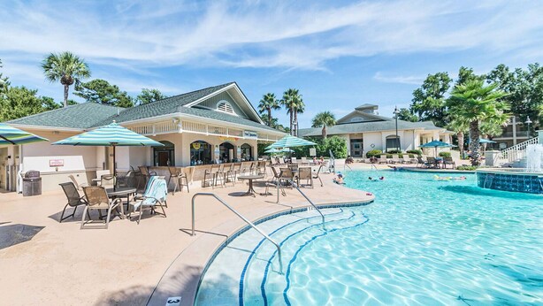 Un espace aménagé au bord de la piscine, avec des chaises longues, des parasols et un bâtiment sur lequel est apposée une enseigne indiquant « The Seaside ».