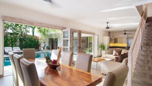 Un comedor amplio con una mesa y sillas de madera, vista a la piscina y una cocina moderna al fondo.