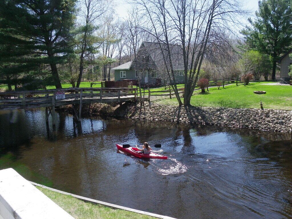 A person kayaking on a calm river with a wooden dock and a house in the background.