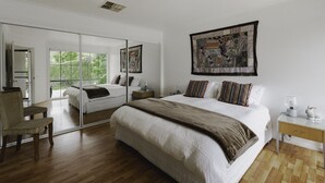 Ein Schlafzimmer mit einem großen Bett, einem Nachttisch, einem Sessel, einem Spiegel und einem großen Fenster.