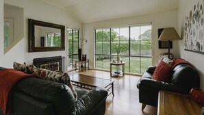 Ein großzügiger Wohnraum mit Kamin, großen Fenstern und Blick auf den Garten.
