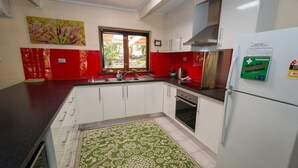 A kitchen with white cabinets, a stainless steel range hood, a refrigerator with a first aid emergency handbook, and a window with a view of greenery.