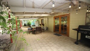 A patio area with a wooden table and chairs, a barbecue grill, and a sliding glass door leading to a garden.
