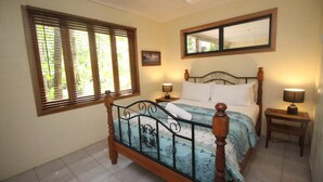A bedroom with a bed, two bedside tables, a window with blinds, a mirror, and a picture on the wall.