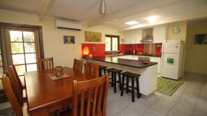 A compact kitchen with a dining area, featuring a central island, a refrigerator, and a clock on the wall.