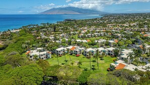 A coastal resort with multiple bungalow-style buildings, a central grassy area, and a view of the ocean and a mountain in the background. - Palms at Wailea  Spectacular Ocean Views with Exceptional Star Rating  (Kihei)