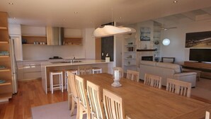 A modern kitchen with a central island, a dining area with wooden chairs, a white sofa, and a TV in the living room. - Rio Grande - views of the bay and the beach (CAMDEN HEAD)