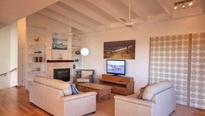 A living room with a fireplace, a television, and a ceiling fan. - Rio Grande - views of the bay and the beach (CAMDEN HEAD)