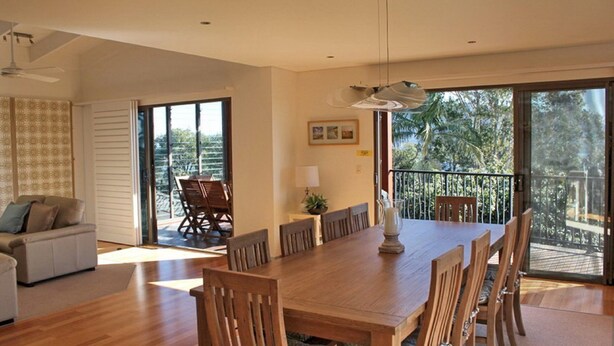 A spacious dining area with a large wooden table and chairs, a sofa, and a balcony with a view of trees. - Rio Grande - views of the bay and the beach (CAMDEN HEAD)