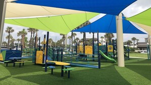 A playground with various play structures, including slides and climbing areas, under a shaded canopy. - Beach front condo with ocean views and community pool. 2/2 on non drive beach.  (New Smyrna Beach)