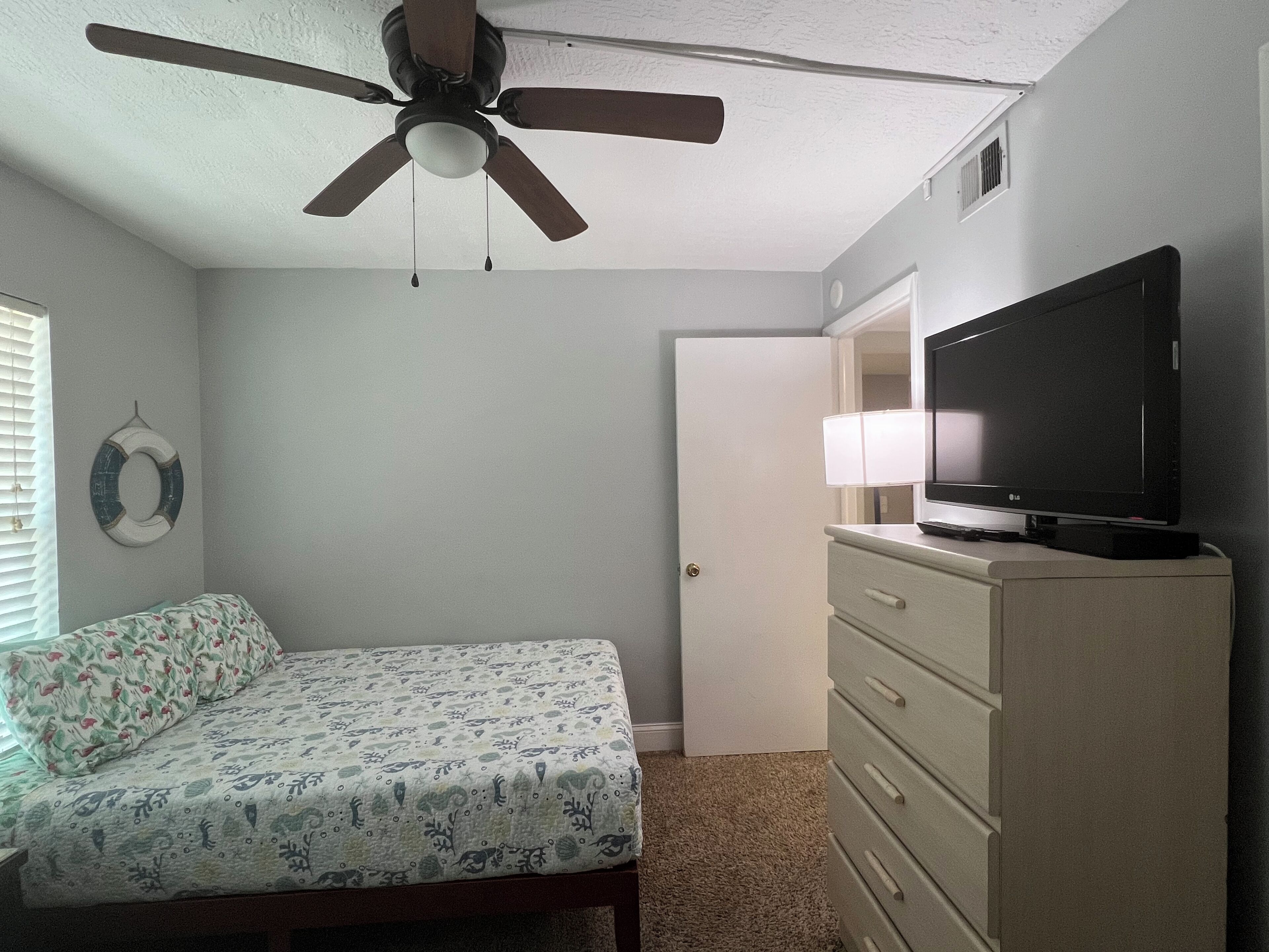 Un dormitorio con cama, cómoda, ventilador de techo y televisor.