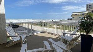 A balcony with white Adirondack chairs and a view of the ocean. - Beach front condo with ocean views and community pool. 2/2 on non drive beach.  (New Smyrna Beach)