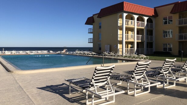 A poolside area with lounge chairs and a building with balconies overlooking the ocean. - Beach front condo with ocean views and community pool. 2/2 on non drive beach.  (New Smyrna Beach)