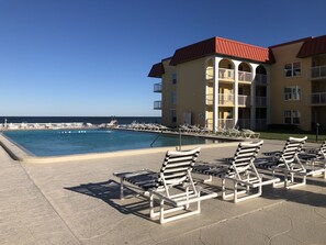 A poolside area with lounge chairs and a building with balconies overlooking the ocean. - Beach front condo with ocean views and community pool. 2/2 on non drive beach.  (New Smyrna Beach)