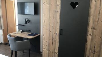 Una habitación con cama, escritorio con silla, armario, televisor y teléfono.