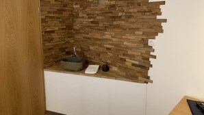 Un baño con pared de mosaico de piedra, puerta de madera y un lavamanos pequeño con una toalla.