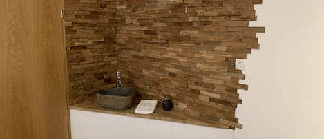 Un baño con pared de mosaico de piedra, puerta de madera y un lavamanos pequeño con una toalla.