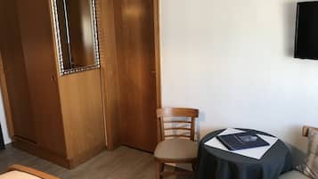 Una habitación de hotel con un armario de madera, una sola silla, una mesa redonda con mantel negro y un televisor montado en la pared.