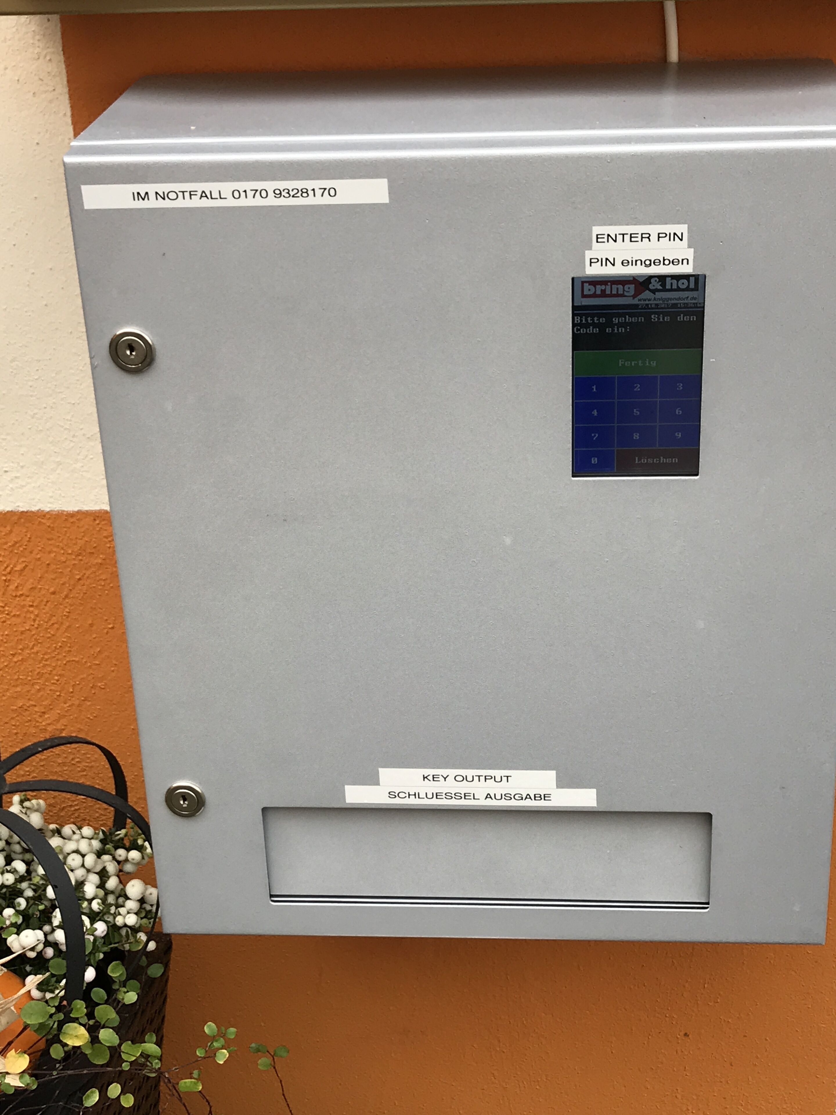 Una caja de seguridad gris con teclado, cerradura y etiquetas en varios idiomas.