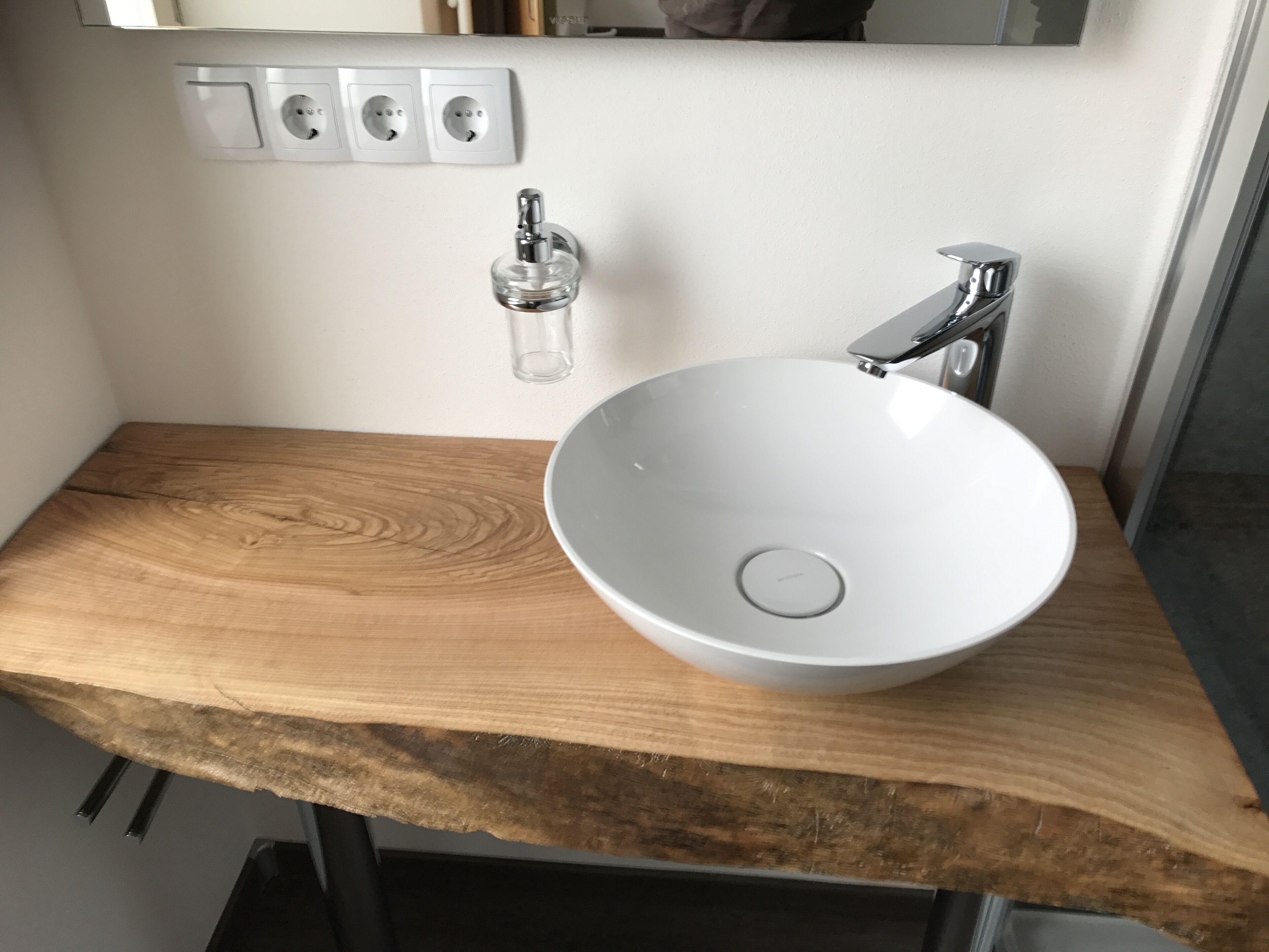 Un baño con encimera de madera, un lavamanos blanco, un espejo y un interruptor de luz en la pared.