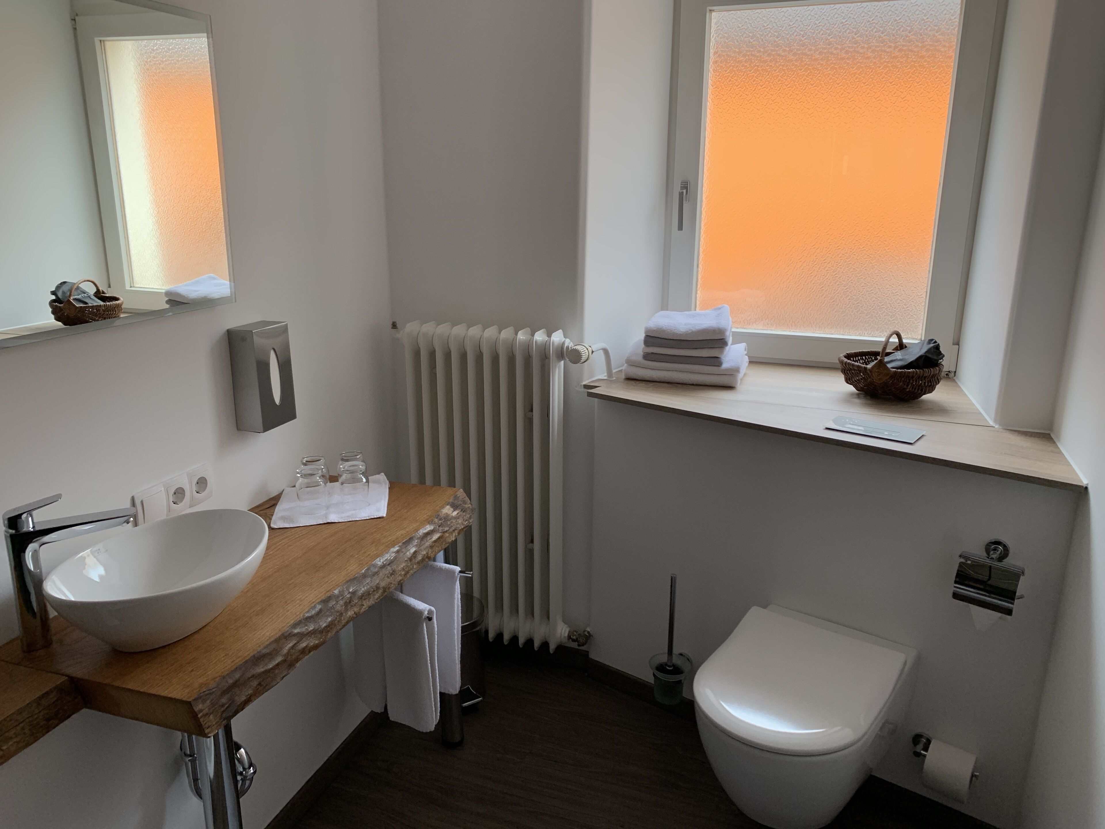 Ein Badezimmer mit einem Holzkosmetikschrank, einem weißen Waschbecken, einer Toilette, einem Heizkörper und einem Fenster mit Blick.