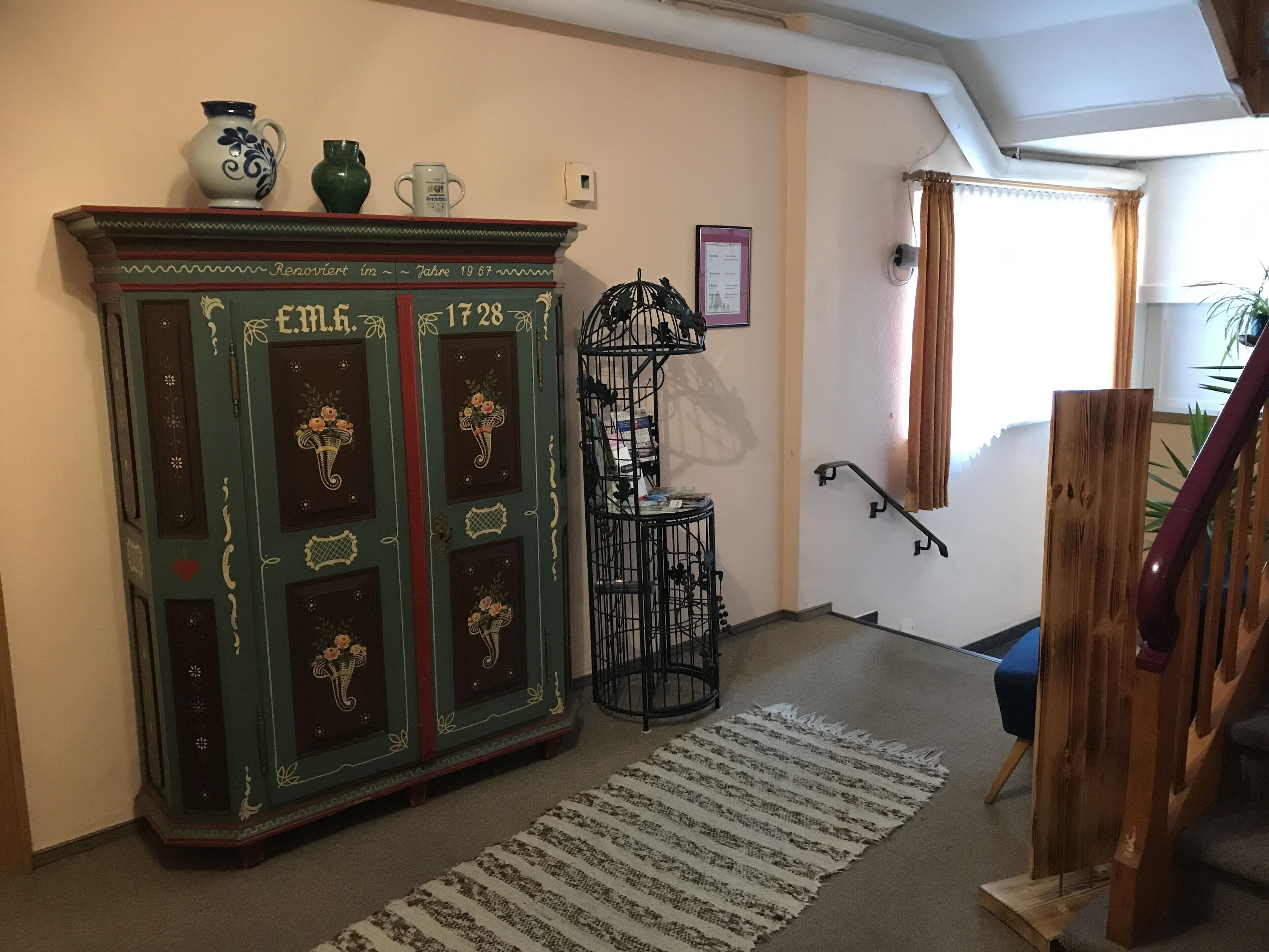 Ein Zimmer mit einem antiken Schrank, einem kleinen Tisch mit einer Vase und einer Treppe.
