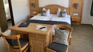 Una habitación de hotel con cama, mesitas de noche, un escritorio con silla y un armario de madera.