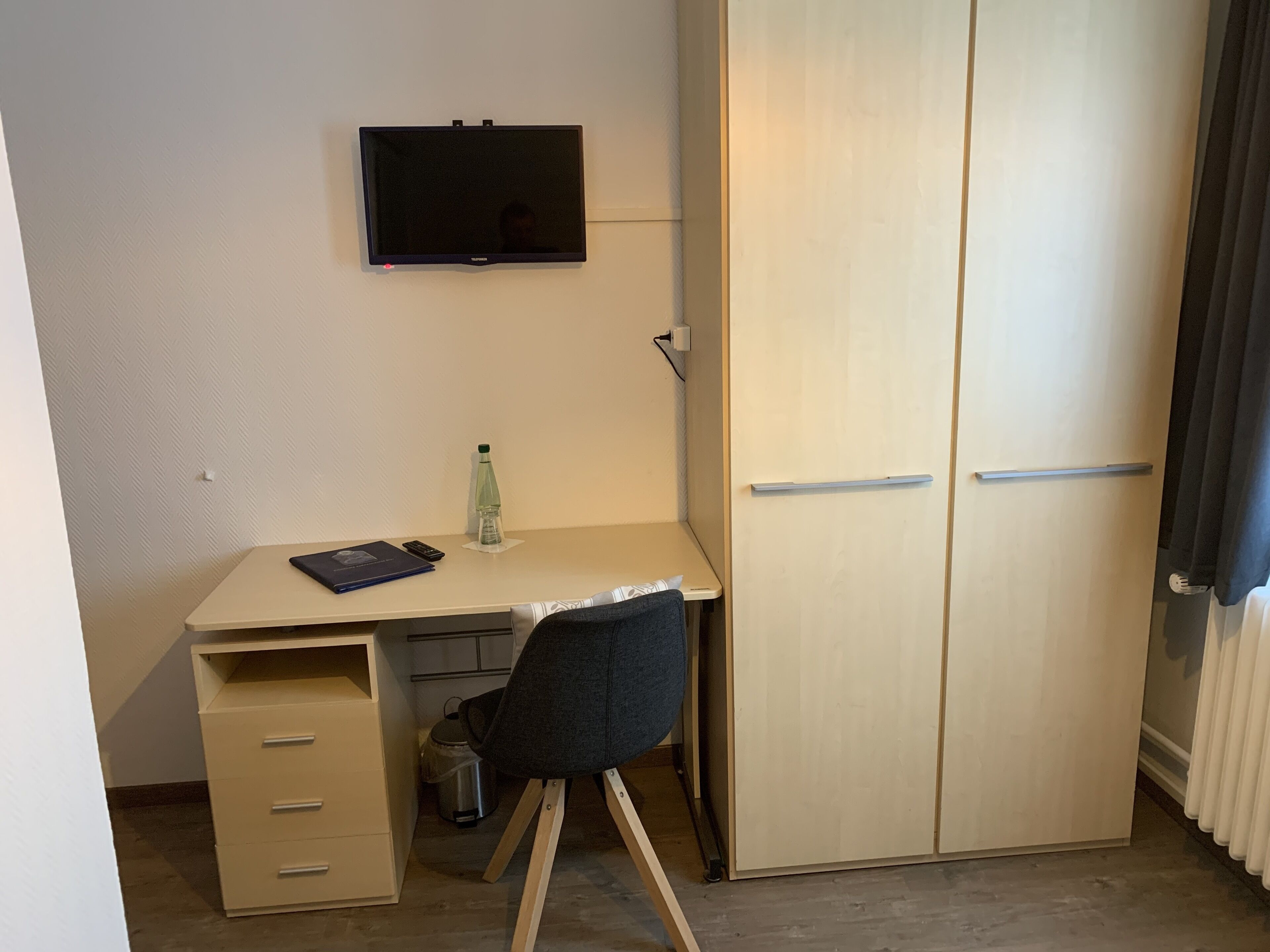 Ein kleiner, kompakter Raum mit Schreibtisch, Stuhl und Kleiderschrank.