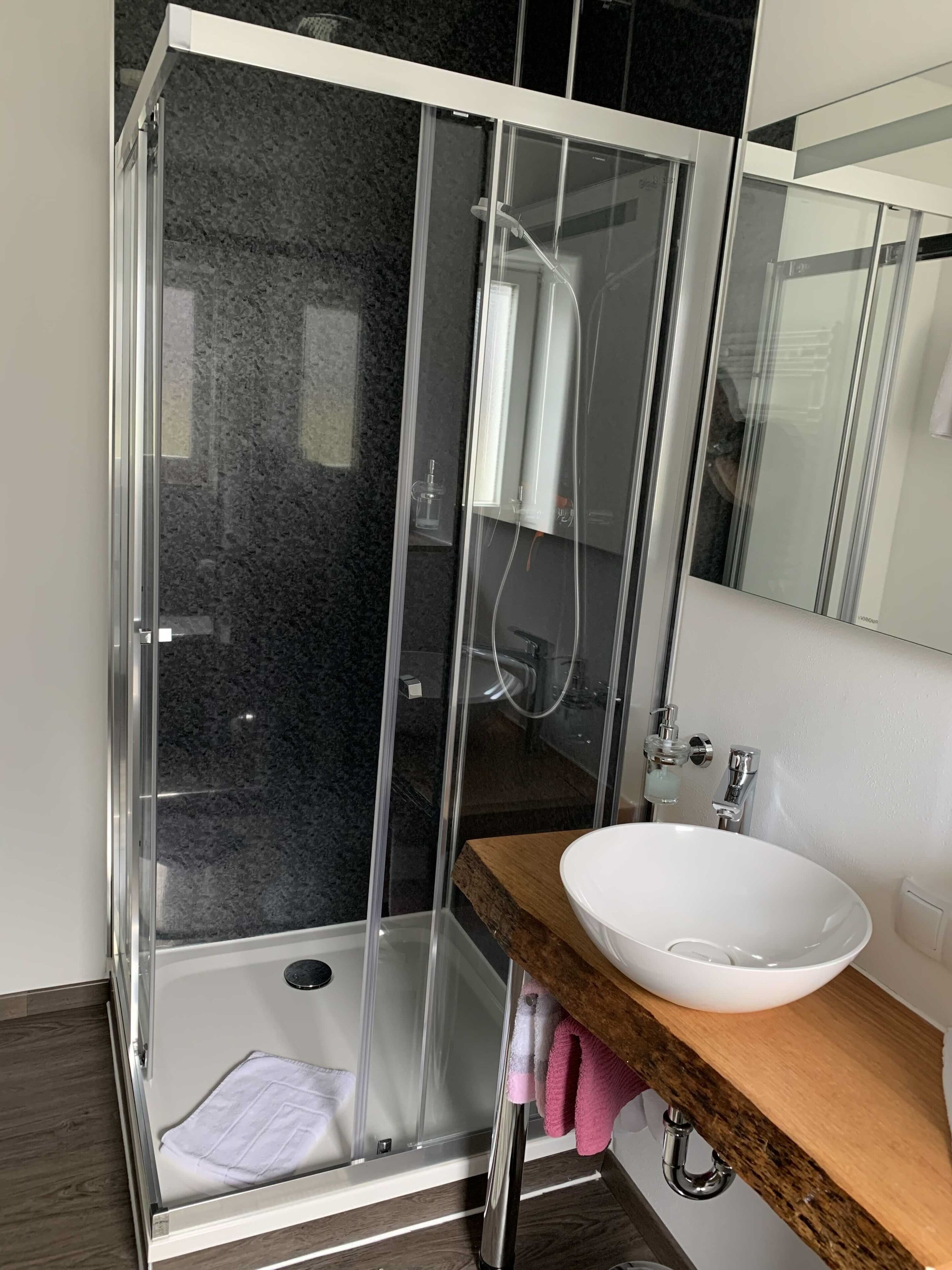 A modern bathroom with a glass-enclosed shower, a wooden vanity, and a white sink.