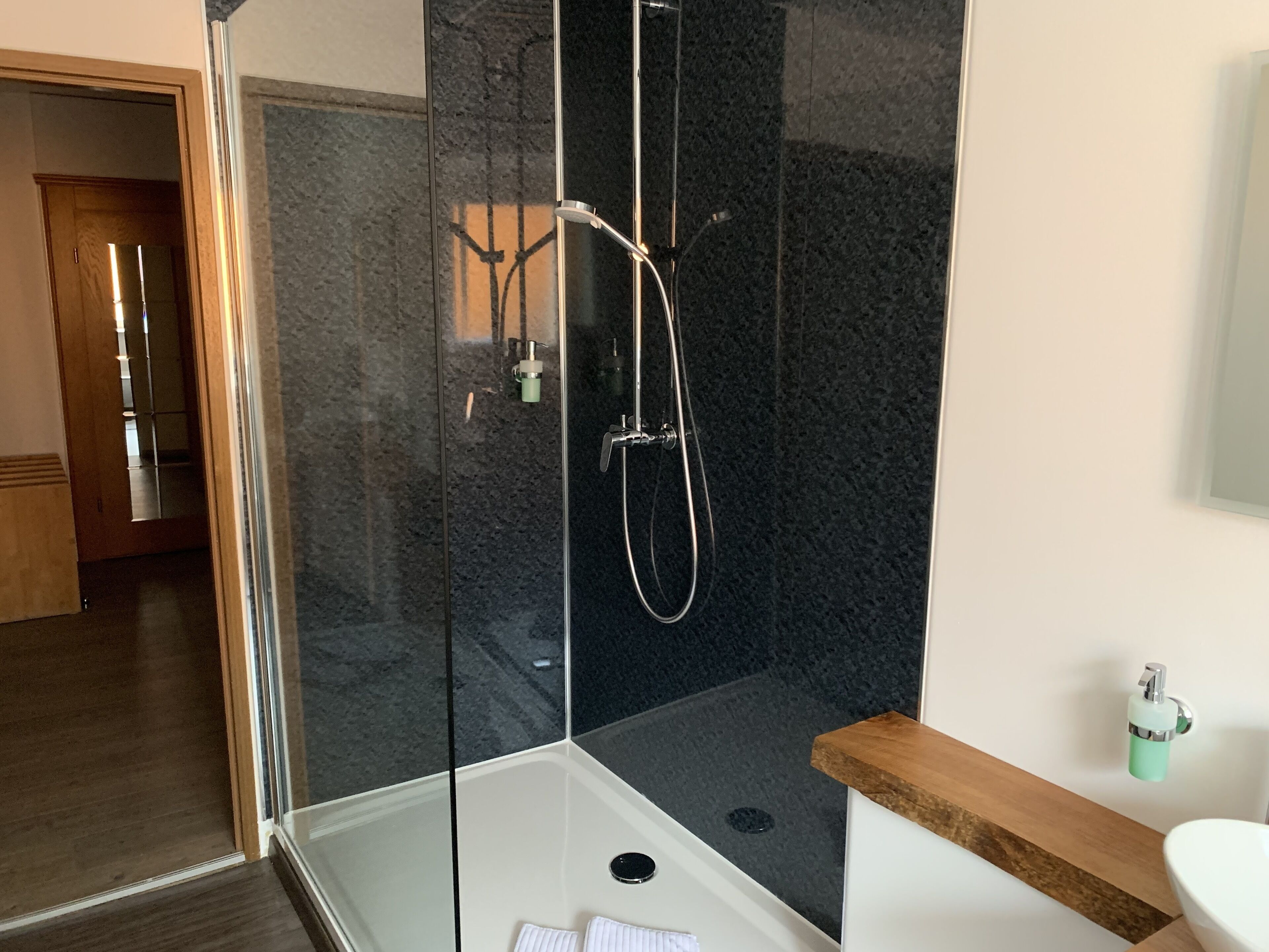 Ein modernes Badezimmer mit einer Duschkabine aus Glas, einem weißen Waschbecken und einem Holzlagerraum.