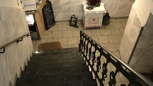Una escalera con barandilla, una mesita con un jarrón de flores y un cartel con texto.