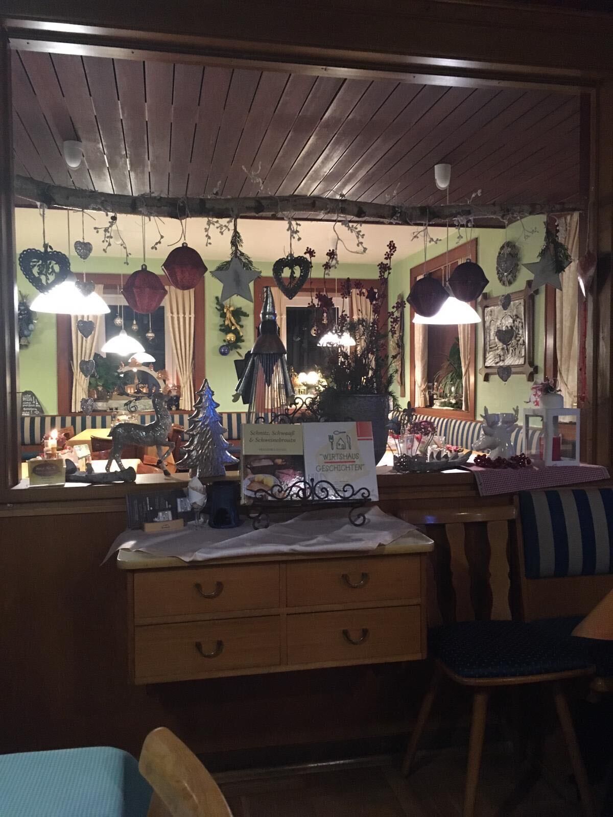 Quarto acolhedor com teto de madeira, uma pequena escrivaninha com gavetas, uma cadeira e diversas decorações, incluindo enfeites pendurados e um pinheiro de Natal.
