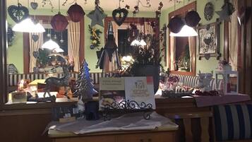Quarto acolhedor com teto de madeira, uma pequena escrivaninha com gavetas, uma cadeira e diversas decorações, incluindo enfeites pendurados e um pinheiro de Natal.
