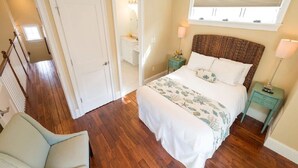 Une chambre à coucher avec un grand lit, une table de chevet, une chaise, une fenêtre avec des stores et une porte donnant sur une autre pièce.