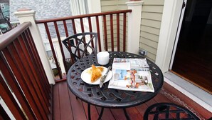 Une petite table ronde avec un journal, une assiette de nourriture et une tasse, le tout posé sur un balcon.