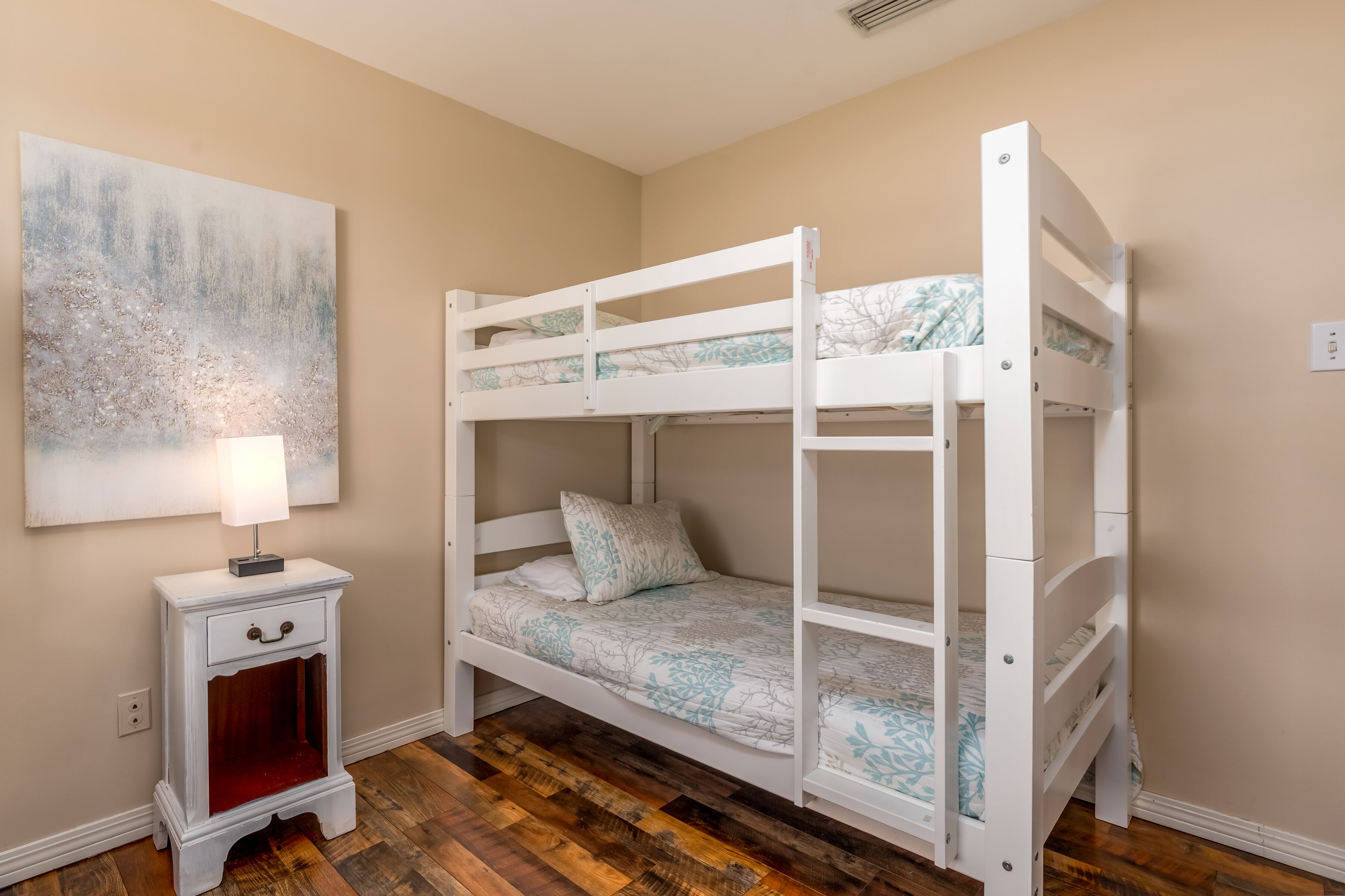 A bunk bed room with a nightstand and a painting on the wall.