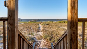 Une terrasse en bois qui mène à une plage, offrant une vue dégagée sur l’océan et sur une jetée située au loin.