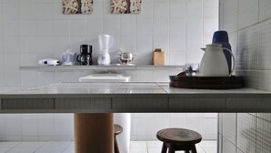 A modern kitchen with white tiles, a coffee maker, a blender, and a kettle on the counter. There are two stools and a small table with a pitcher. - Beachfront house with pool and Wi-Fi in Praia Azul - Pitimbu/PB (pitimbu)