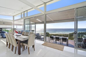 Un intérieur moderne avec un coin repas, de grandes fenêtres et une vue sur l’océan.