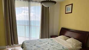 Un dormitorio con cama, cortinas, una mesita de noche y vistas al océano.