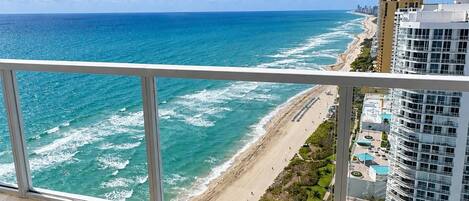 A balcony with a view of the ocean and a beach, overlooking a high-rise building.