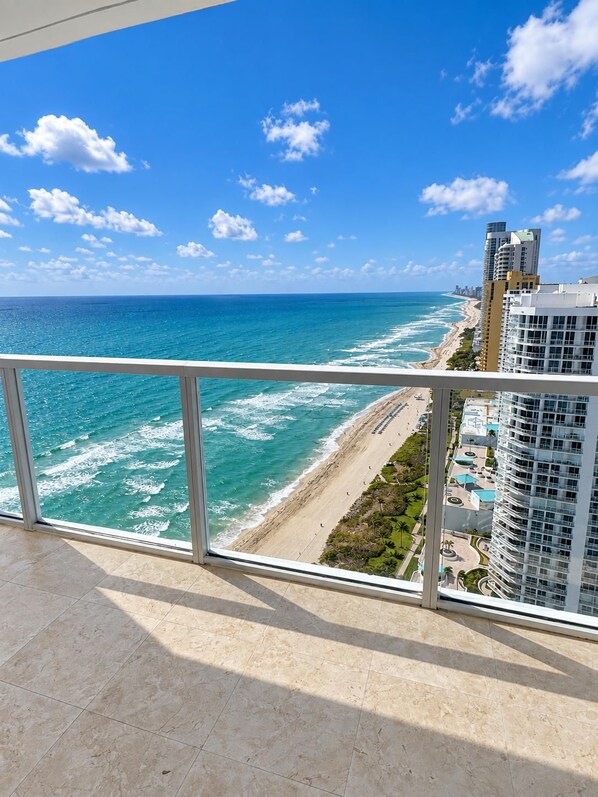 A balcony with a view of the ocean and a beach, overlooking a high-rise building. - Beachfront Luxurious Paradise - LaPerla - Direct Ocean View in Sunny Isles (Sunny Isles)