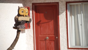 A wooden owl holding a sign that says "BIENVENIDO" in front of a red door and window.