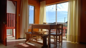 A room with a wooden bench, a table, and a view of the outdoors through large windows.
