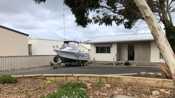 Un bateau sur une remorque, devant une maison avec un garage et un petit porche.